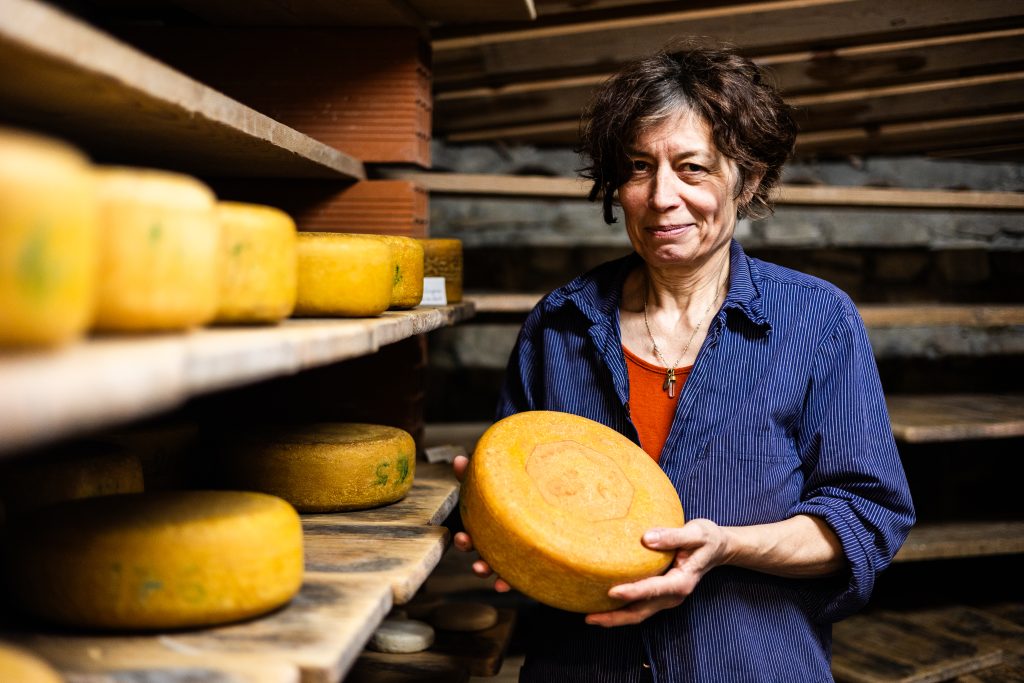 Monika est éleveuse de brebis de race Manech Tête Noire et Rousse dans les Corbières où elle produit du fromage de brebis. Monika, agricultrice et fromagère dans son atelier de séchage avec une tome de brebis.